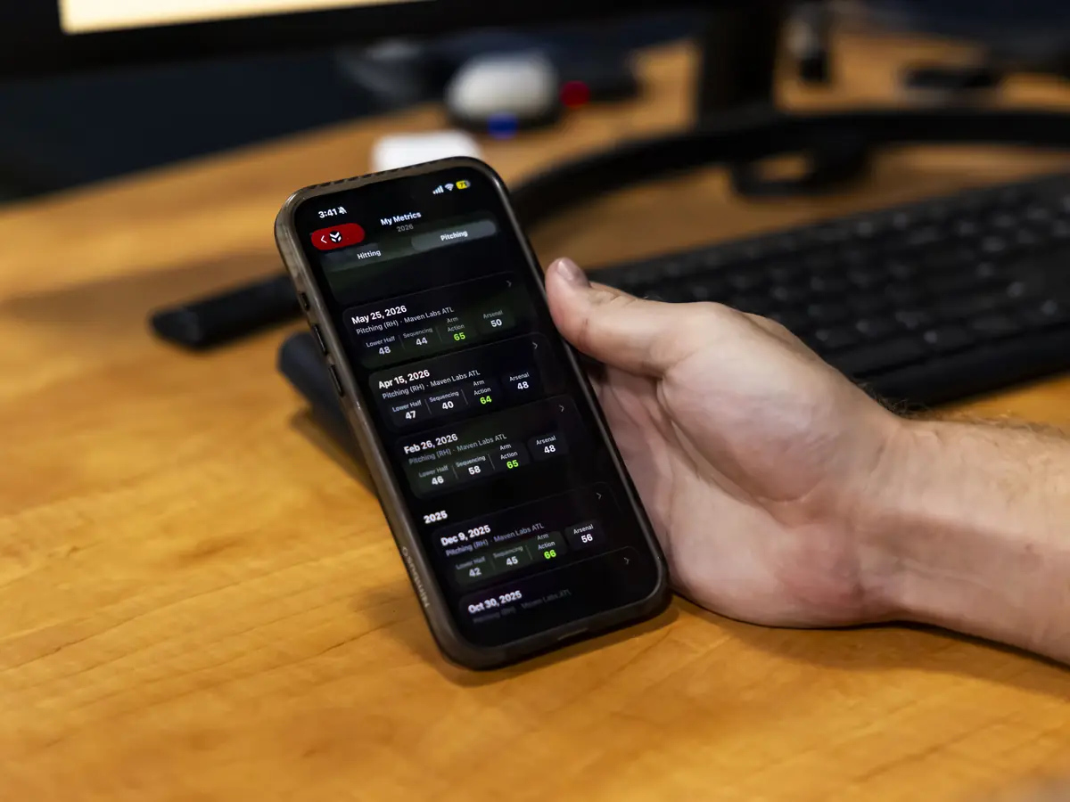 A hand holding a phone with the Maven App open beside a monitor of assessment data